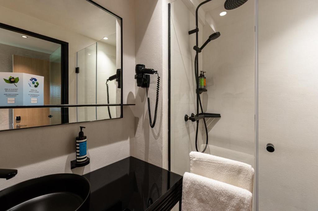 Mūsdienīga vannas istaba ar melnu izlietni, spoguli un dušas kabīni. Interjerā ir redzami higiēnas izstrādājumi un dvielis.