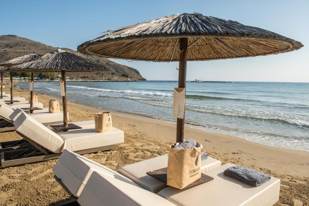 Pludmales atpūtas zona ar saulessargiem un guļamkrēsliem, kas novietoti pie mierīgām viļņiem. Pievilcīgs skats uz jūru un kalnu fonu.