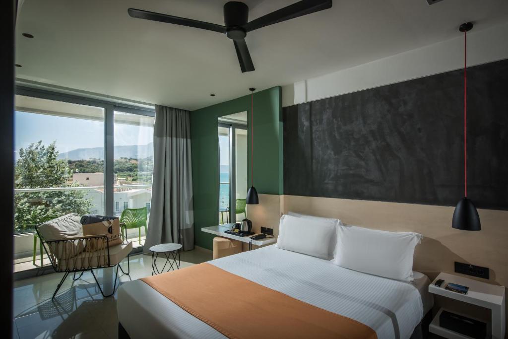 Mūsdienīga viesnīcas numura iekārtojums ar skatu uz jūru, ietver gultu ar oranžu segumu un ērtu atpūtas zonu. Interjers ir gaišs un stilīgs, ar lieliem logiem, kas nodrošina dabīgu apgaismojumu.