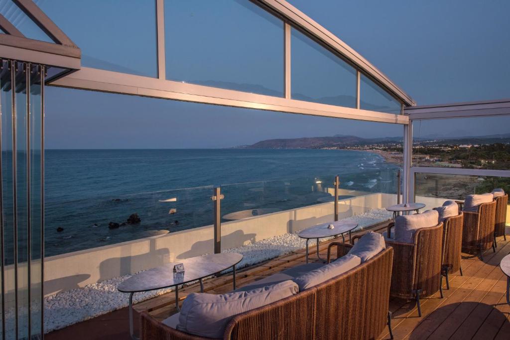 Jūras piekrastes terase ar mīkstiem krēsliem un skatu uz saulrietu, radot relaksējošu atmosfēru un izsmalcinātu pieredzi.