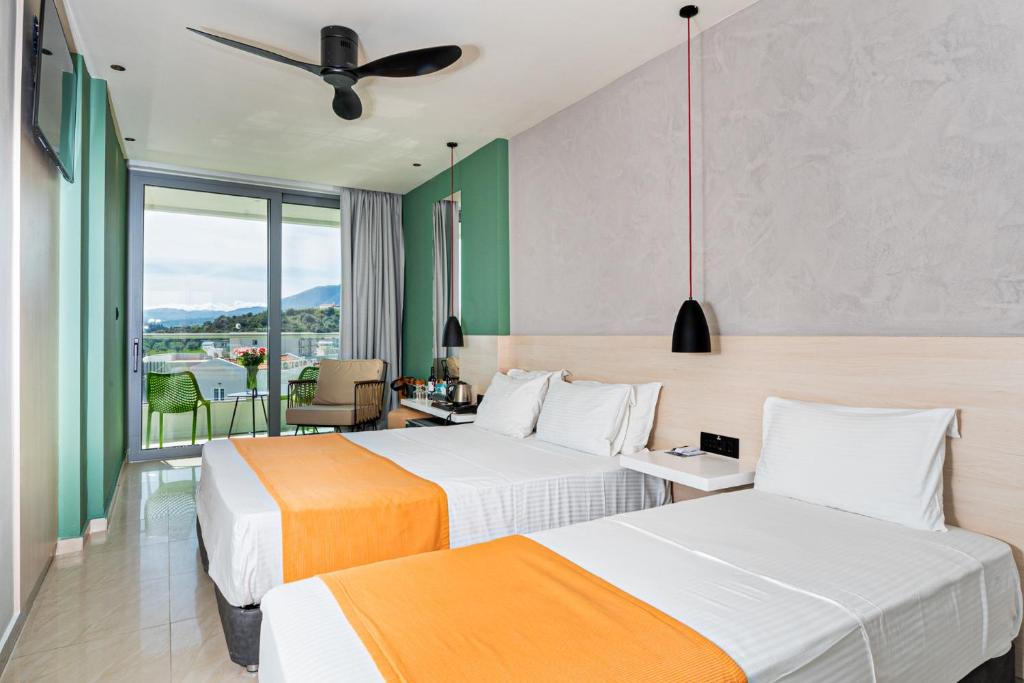 Mūsdienīga viesnīcas numura iekārtojums ar divām gultām un skatu uz kalniem. Numurā ir balkons ar zaļām mēbelēm un modernais apgaismojums.