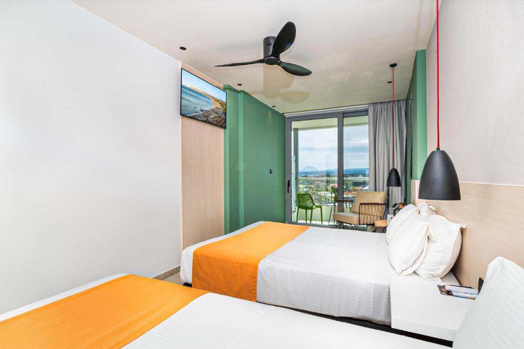 Mūsdienīga viesnīcas numuriņa interjers ar divām gultām un skatu uz dabu. Telpā ir televizors, ventilators un ērta atpūtas zona ar dārza mēbelēm.