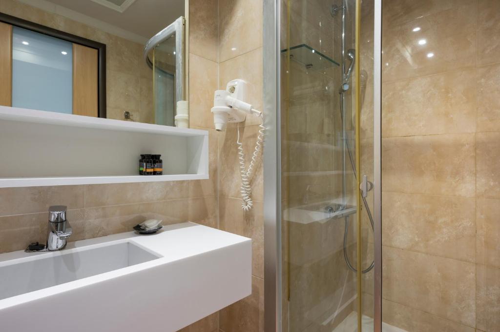 Moderns vannas istabas interjers ar stikla dušu, pelēkajiem flīzēm un minimālistisku izlietni. Uz plauktiņa redzami dažādi higiēnas produkti.