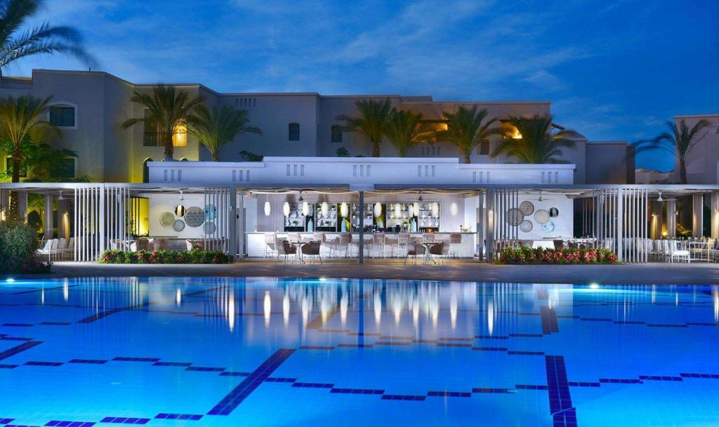 Steigenberger Alcazar viesnīcas baseins ar bāru piekrastē vakarā.