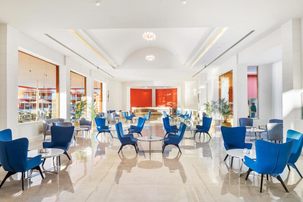 Mūsdienīga viesnīcas uzgaidāmā zona ar zilu mīksto mēbeļu komplektu un elegantiem galdiņiem, kas nodrošina ērtu atmosfēru. Gaismas un plašums rada patīkamu un relaksējošu vidi.
