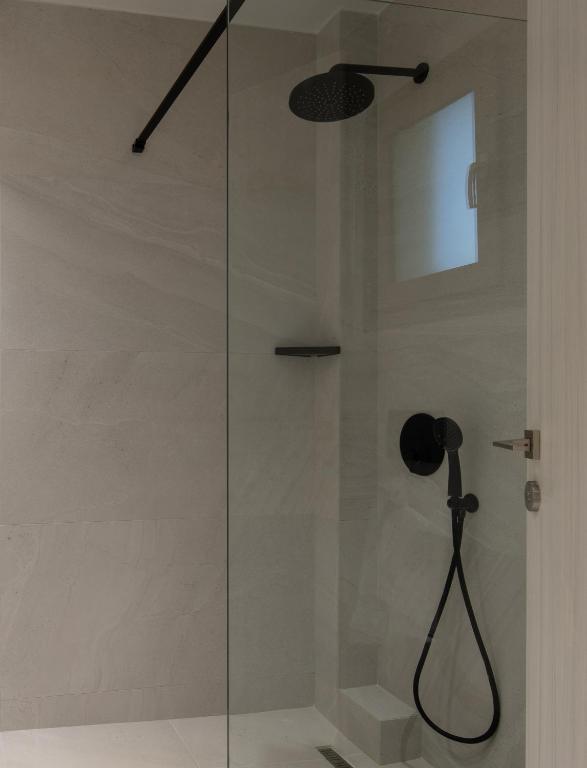 Mūsdienīga dušas telpa ar stikla kabīni un melnu dušas galvu, akcentējot pelēkas flīzes un minimālisma dizainu. Ideāla vieta relaksācijai un komfortam.