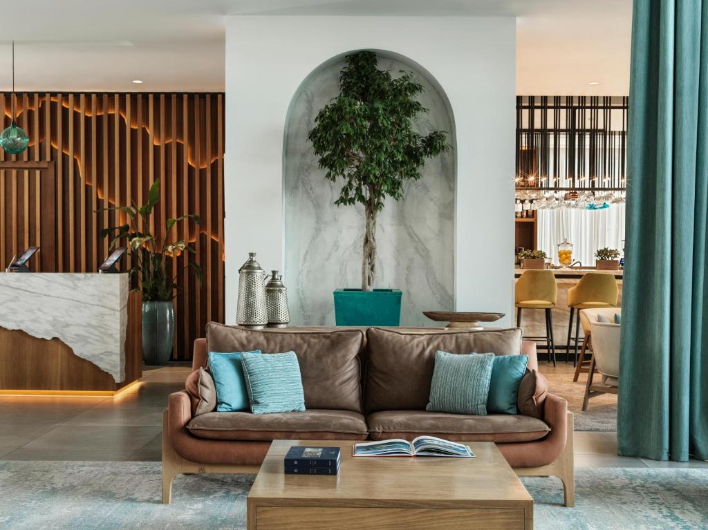Mūsdienīgs viesnīcas interjers ar ērtu dīvānu, dekoratīvu augu un elegantu bāra zonu, izceļot siltas krāsas un stilīgu dizainu.