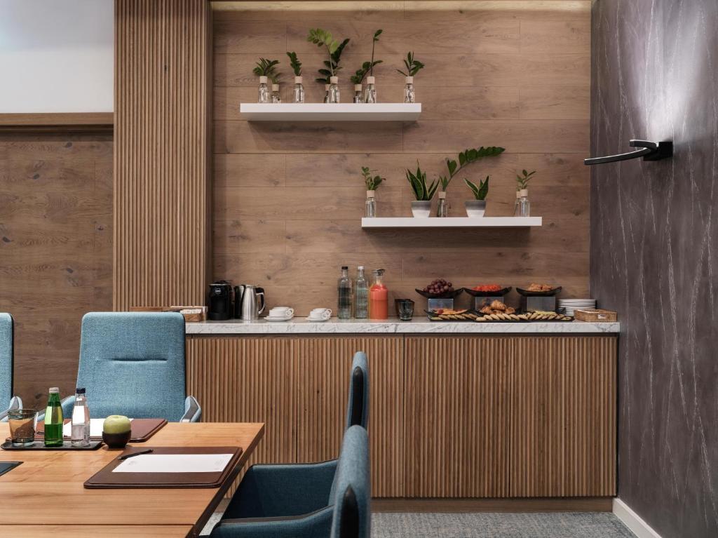 Mūsdienīga sanāksmju telpa ar koka apdari, augiem uz plauktiem un viesmīlīgu uzkodu galdu. Gaisīga atmosfēra ar elegantiem mēbeļu elementiem.