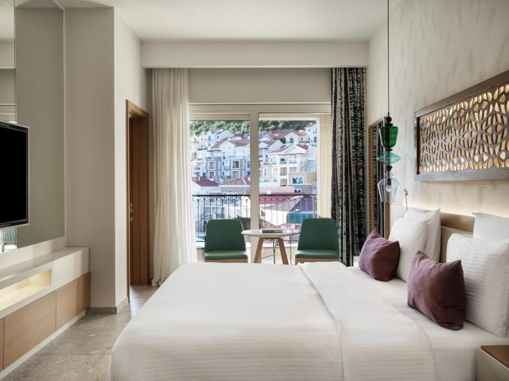 Moderns viesnīcas numurs ar plašu logu, no kura paveras skats uz pilsētu. Interjers ir elegants ar gultu, televizoru un ērtām mēbelēm.