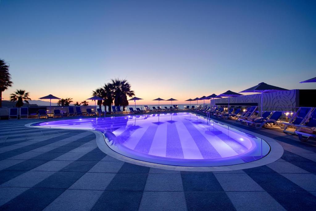 Arina Beach Resort baseins ar zilu apgaismojumu piekrastē saulrieta laikā
