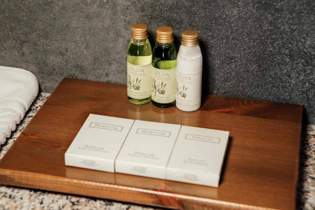 Vannas istabas piederumu komplekts, kas ietver šampūnu, ķermeņa losjonu un vannas cepuri, izkārtots uz koka paletes.