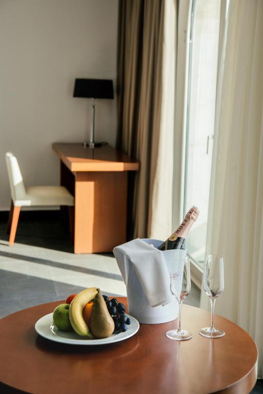 Svaigi augļi un šampanietis uz galda, kamēr fona interjerā redzams darba galds un krēsls. Ideāla viesnīcas atmosfēra relaksācijai.