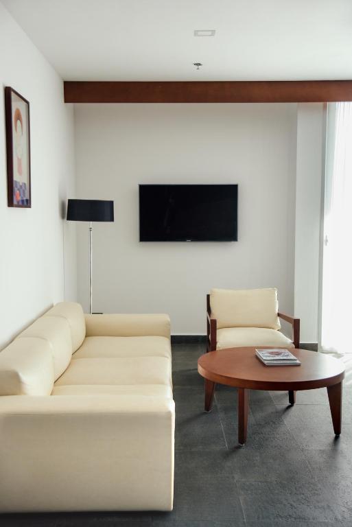 Mūsdienīgs viesistabas interjers ar gaišām mēbelēm, melnu televizoru un koka galdu, kas izvietots uz tumša grīdas.