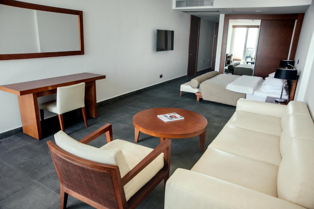 Liela un moderna viesnīcas istaba ar vieglu krēslu, dīvānu un koka galdu, kas izveidota relaksējošai atmosfērai. Interjers ir stilīgs un minimāls, ar dabīgām krāsām un plašu telpu.