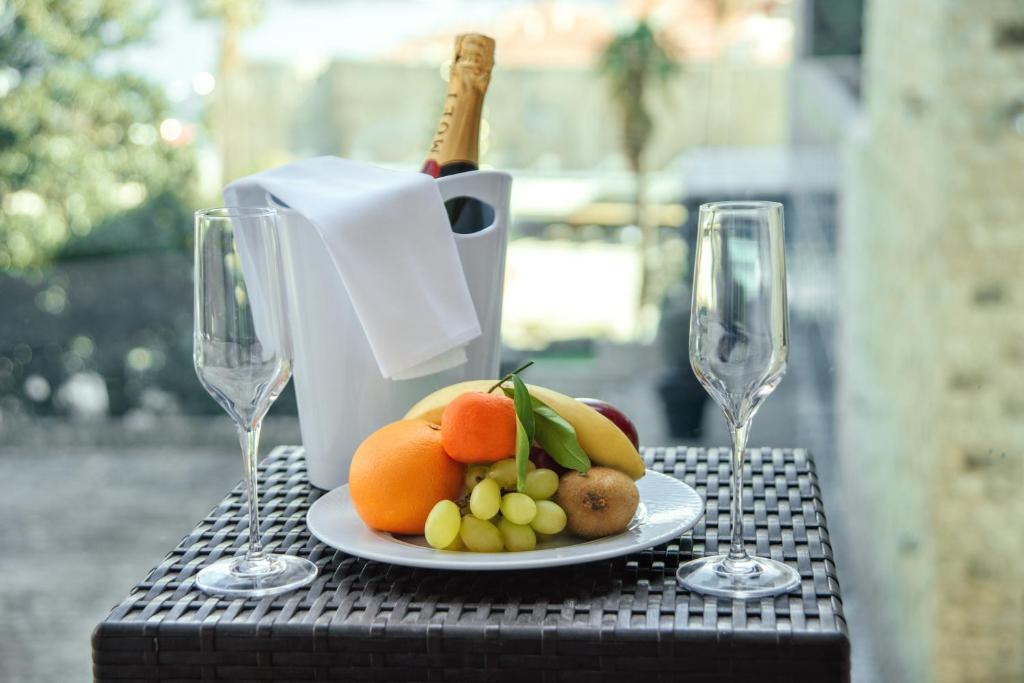 Gludā galdā ir augļu šķīvis ar apelsīniem, banāniem un vīnogām, blakus divi šampanieša glāzes un ledus spainis ar šampanieti.