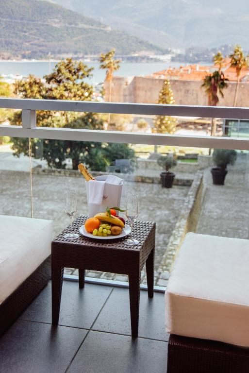 Balkona skats ar augļu šķīvi un šampanieša glāzēm uz galda, kamēr fonā redzama gleznaina ainava ar kalniem un jūru.