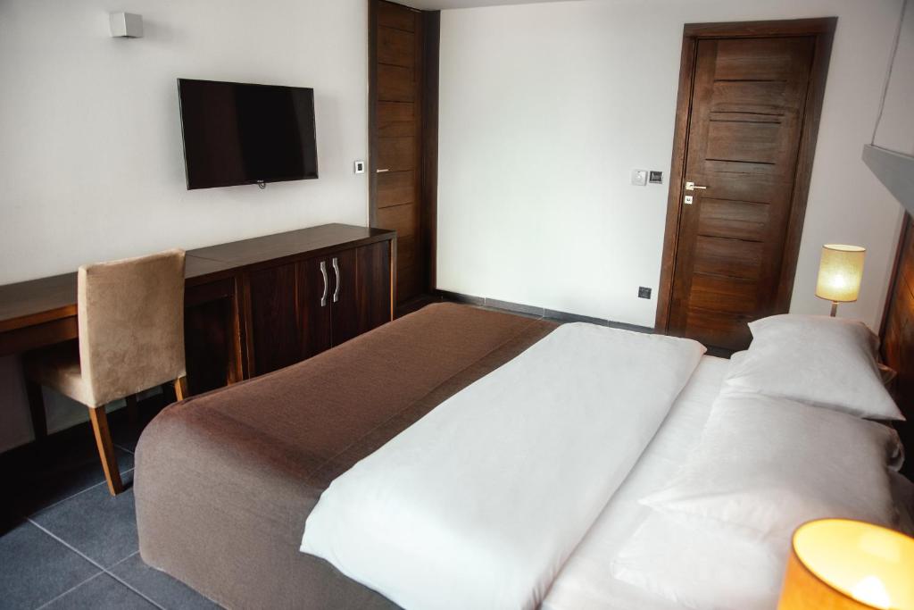 Moderns viesnīcas numurs ar divguļamo gultu, koka mēbelēm un televizoru. Numurā ir arī rakstāmgalds un gaismas avots.