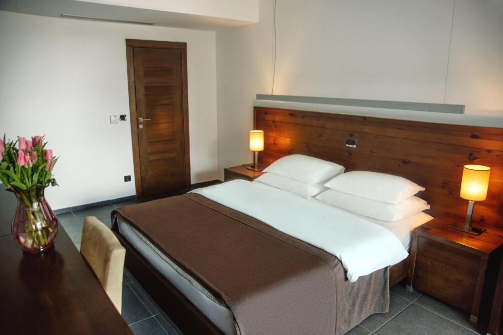 Mūsdienīgs guļamistabas interjers ar divguļamo gultu, koka galdiem un ziedu kompozīciju uz galda. Siltas apgaismojuma detaļas piešķir telpai mājīgu atmosfēru.