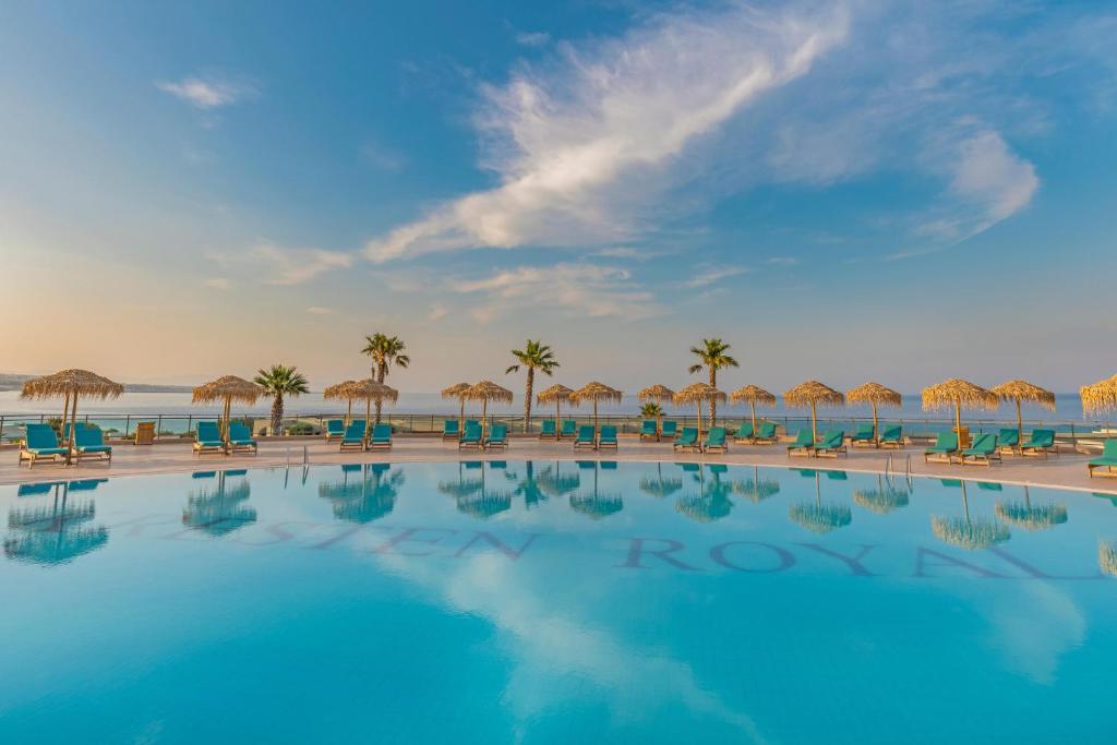 Kresten Royal Euphoria Resort baseins ar palmām un saulessargiem pie jūras.
