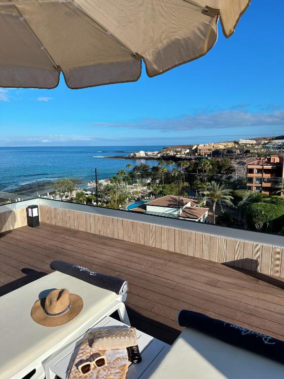 Skats uz okeānu no terases ar sauļošanās krēsliem, saules vāku un pludmales piederumiem. Aiz tā redzami viesnīcu kompleksi un palmām apauguši krasti.