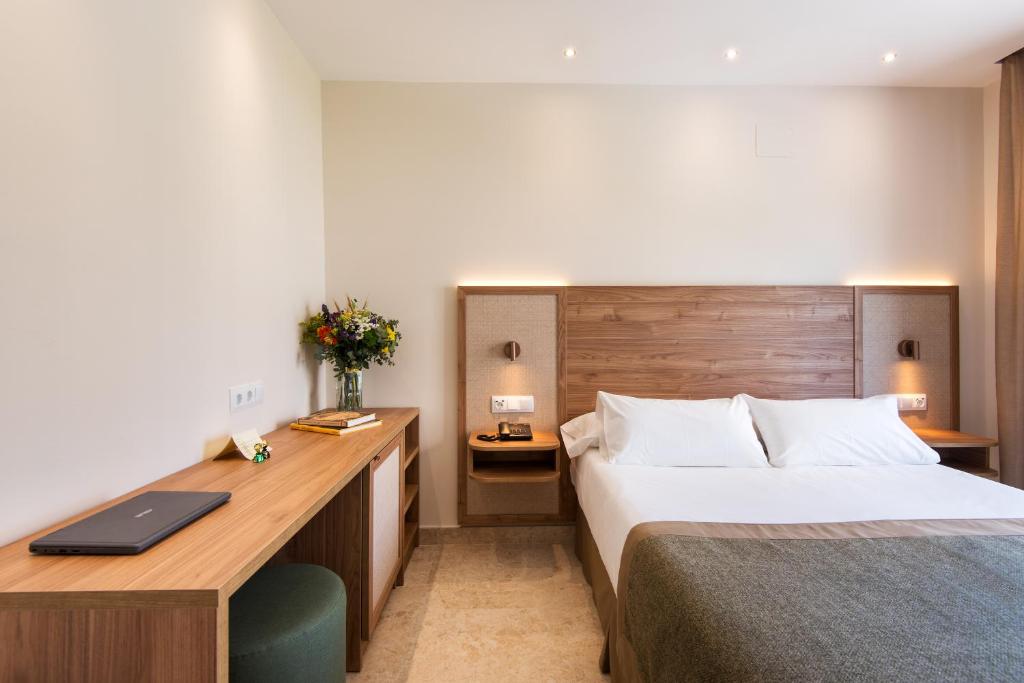 Mūsdienīga viesnīcas numura interjers ar koka mēbelēm, gultu un ziedu kompozīciju uz galda. Numurā ir arī dators un grāmatas uz rakstāmgalda.