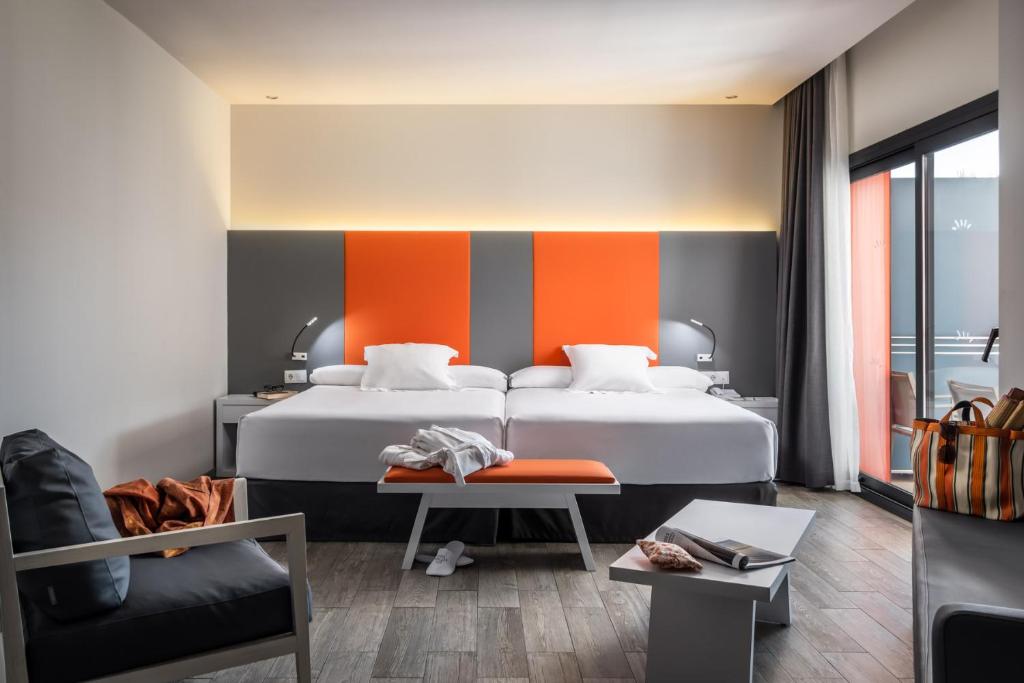 Mūsdienīgs viesnīcas numurs ar divām gultām, gaišām krāsām un akcentiem oranžā tonī. Interjers ietver ērtu sēdekli, galdu un piekļuvi terasei.