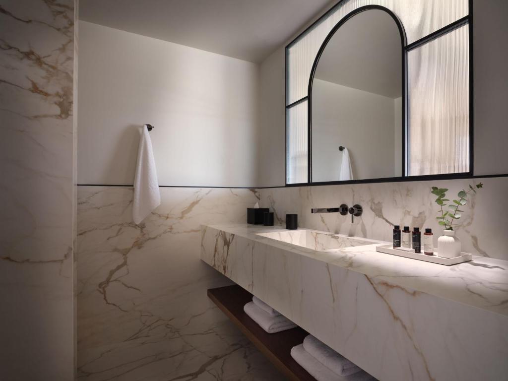Mūsdienīgs vannas istabas dizains ar marmora apdari, elegantu spoguli un minimālu dekoru. Telpa ir gaiša un svaiga, radot relaksējošu atmosfēru.