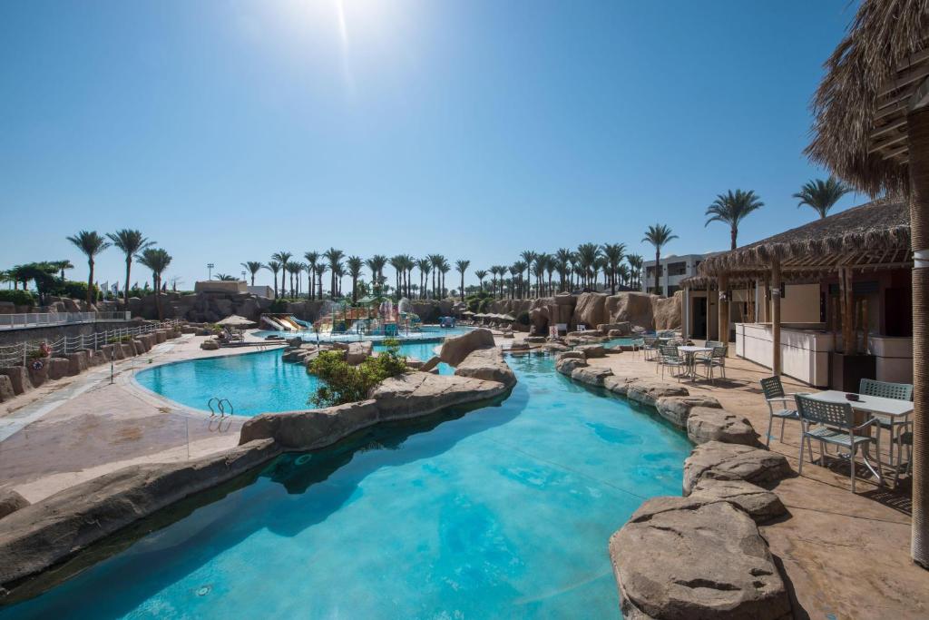 Peldbaseins pie Reef Oasis Beach Resort ar palmām un akmens struktūrām.