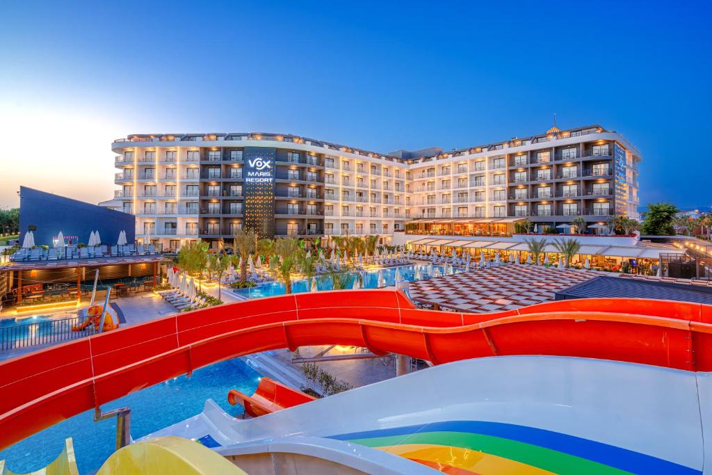 Vox Maris Resort viesnīca ar ūdens slidkalniņiem un peldbaseinu, apgaismota vakarā, radot patīkamu atpūtas atmosfēru. Ideāla vieta ģimenēm un atpūtniekiem, kas meklē komfortu un izklaidi.