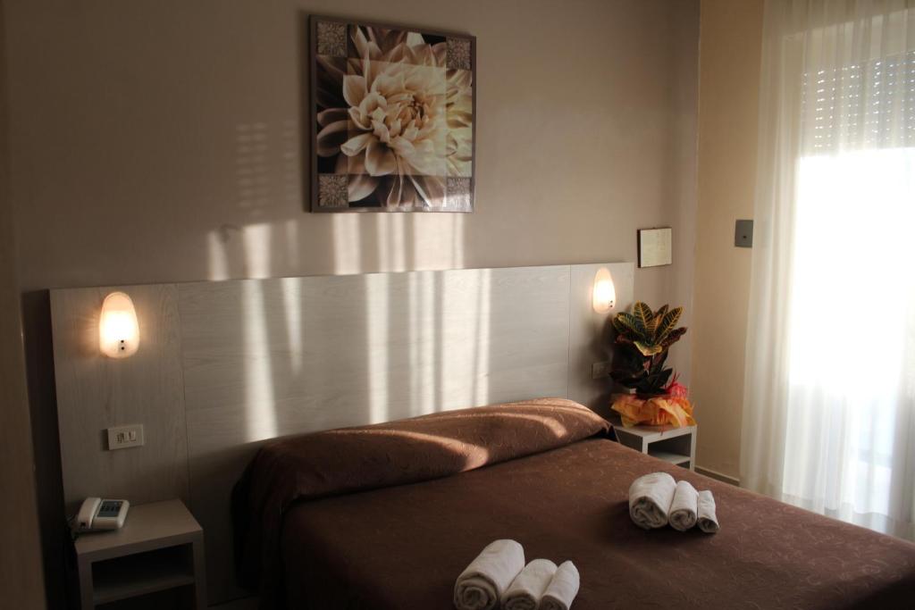 Mājīga viesnīcas numuriņa iekārtojums ar gultu, gaismas avotiem un dekoratīviem elementiem, piemēram, augu un mākslas darbu uz sienas. Rūpīgi salocītas dvieļi uz gultas piešķir numuriņam viesmīlīgu izskatu.