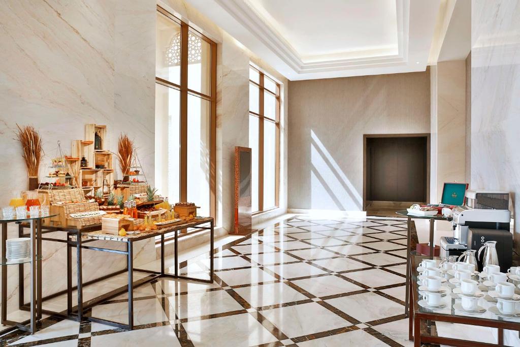 Elegants viesnīcas izstāžu stūris ar dažādiem ēdieniem un dzērieniem, kas sakārtoti uz galdiem. Labi apgaismota telpa ar modernu interjeru un greznu grīdu.