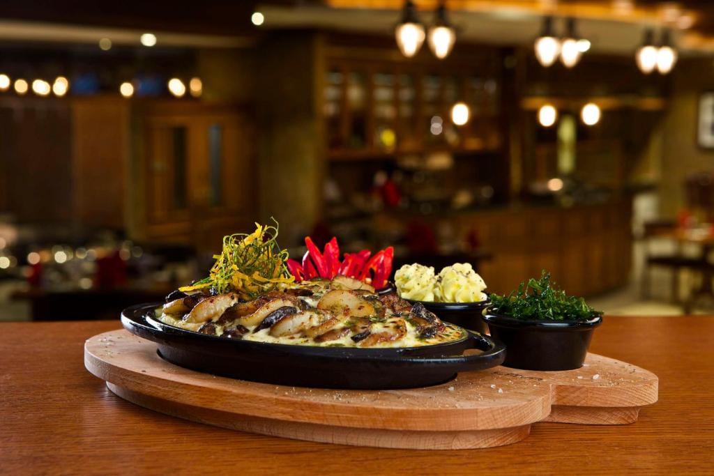 Siltā ēdiena porcija uz melnas pannas, dekorēta ar sarkaniem čili pipariem, garnelēm un zaļumiem, kopā ar kartupeļu biezeni. Fonā redzama eleganta restorāna atmosfēra.