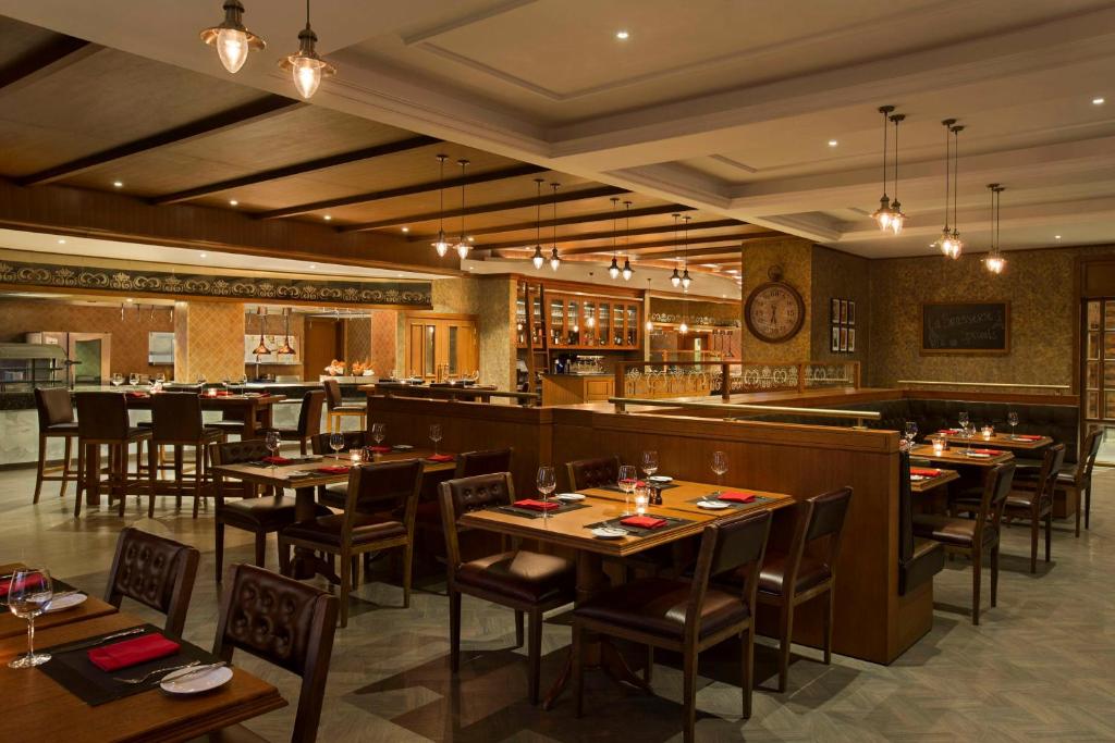 Elegants restorāns ar koka interjeru, kas ietver ēdināšanas zonas ar galdiem un krēsliem, atmosfēra ir silta un viesmīlīga. Gaismas elementi piešķir patīkamu apgaismojumu.