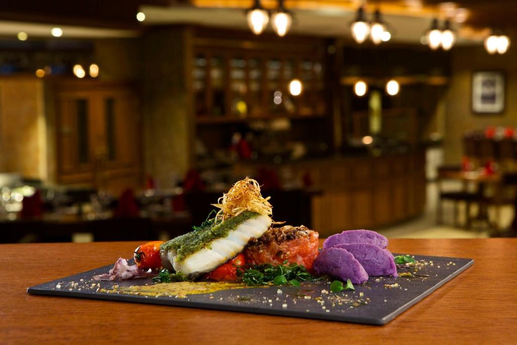 Gurķu ēdiens ar ceptu zivi, zeltainiem tomātiem un violetām kartupeļu biezeņa porcijām uz melnas šķīvju. Daba eleganta restorāna fons.