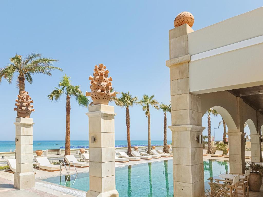 Grecotel Plaza Beach House baseins ar skatu uz piekrasti un palmām.