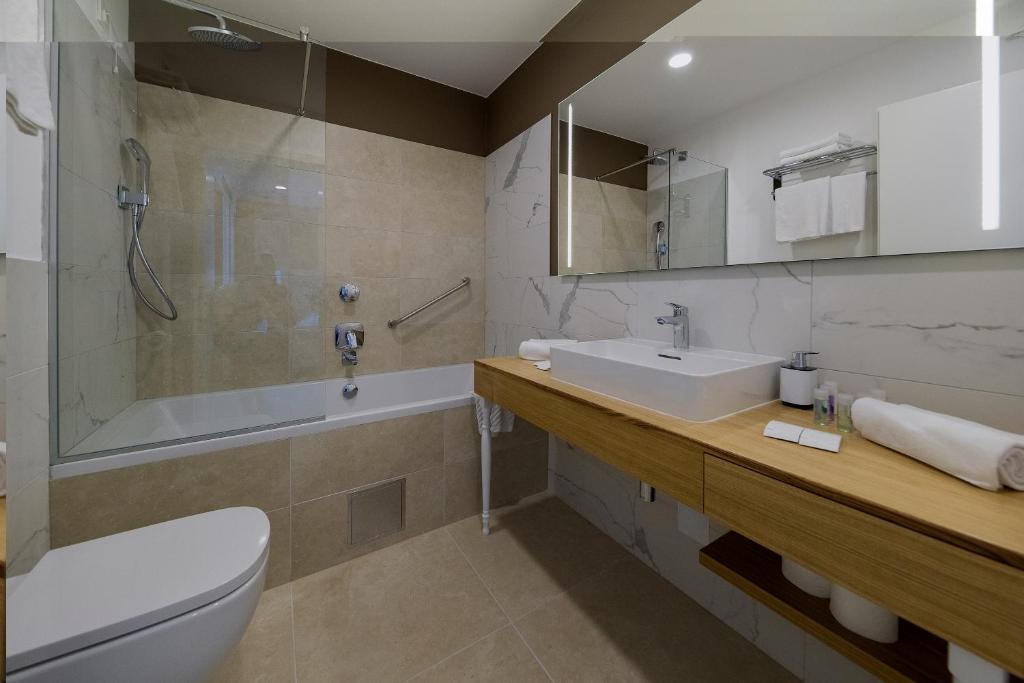 Moderns vannas istabas interjers ar stikla dušu, vannu un koka izlietni, kas papildina eleganto dizainu. Vannas istaba ir gaiša un funkcionāla, ar mūsdienīgām iekārtām un aksesuāriem.