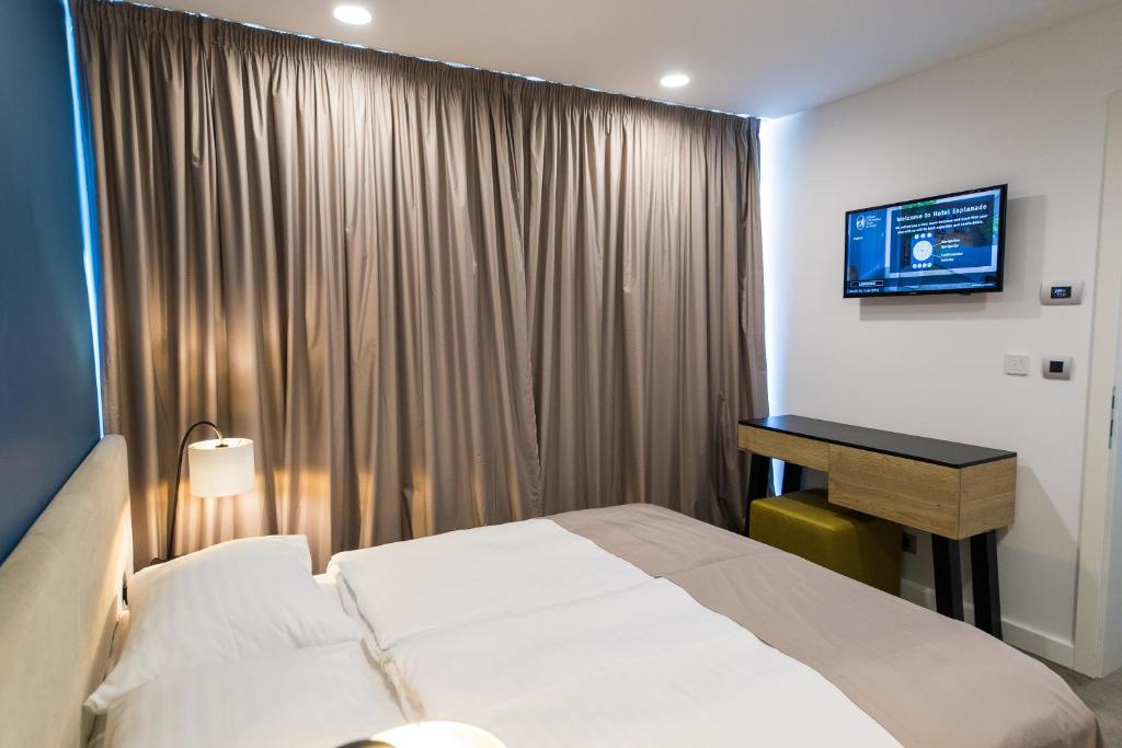 Mūsdienīga viesnīcas istaba ar divguļamo gultu, televizoru un elegantu mēbeļu komplektu. Gaismas un aizkari piešķir telpai siltu atmosfēru.