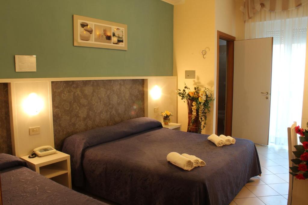 Mūsdienīga viesnīcas numura iekārtojums ar divām gultām, zilu gultasveļu un dekoratīviem elementiem. Telpā ir arī ziedi un gaiša gaisma, kas rada patīkamu atmosfēru.