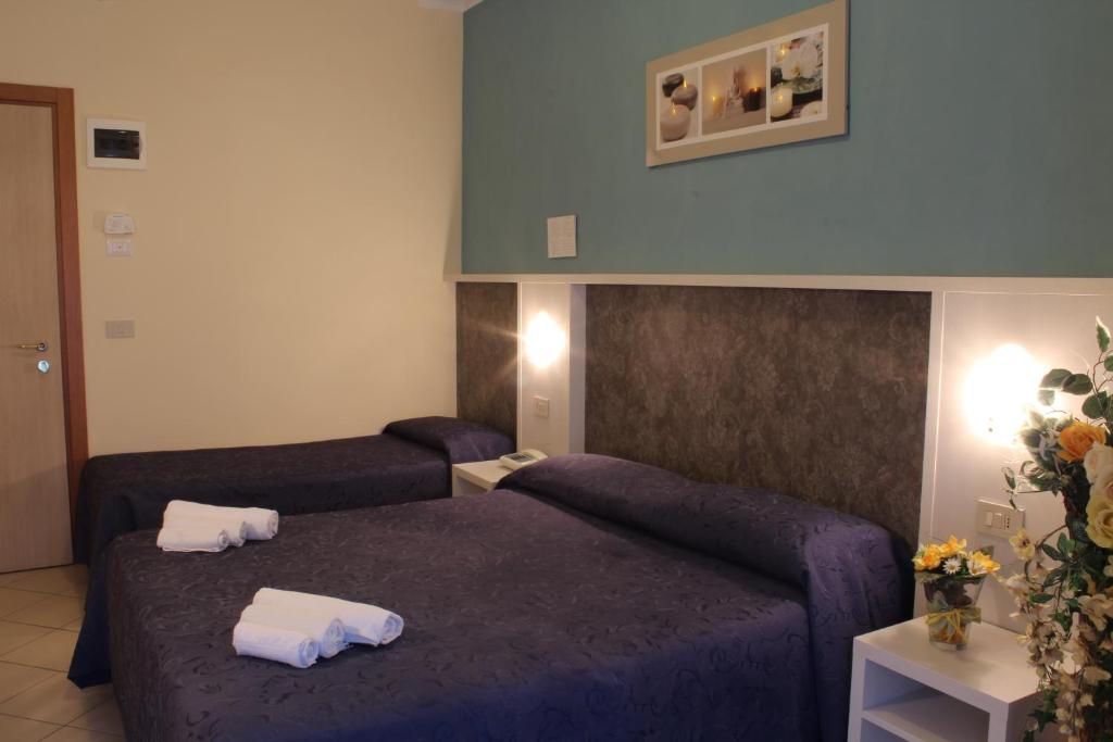 Mūsdienīgs viesnīcas numurs ar divām gultām, tumši zilām gultas veļām un elegantiem apgaismojuma elementiem. Numurā ir arī dekoratīvi ziedi un mākslas darbs uz sienas.