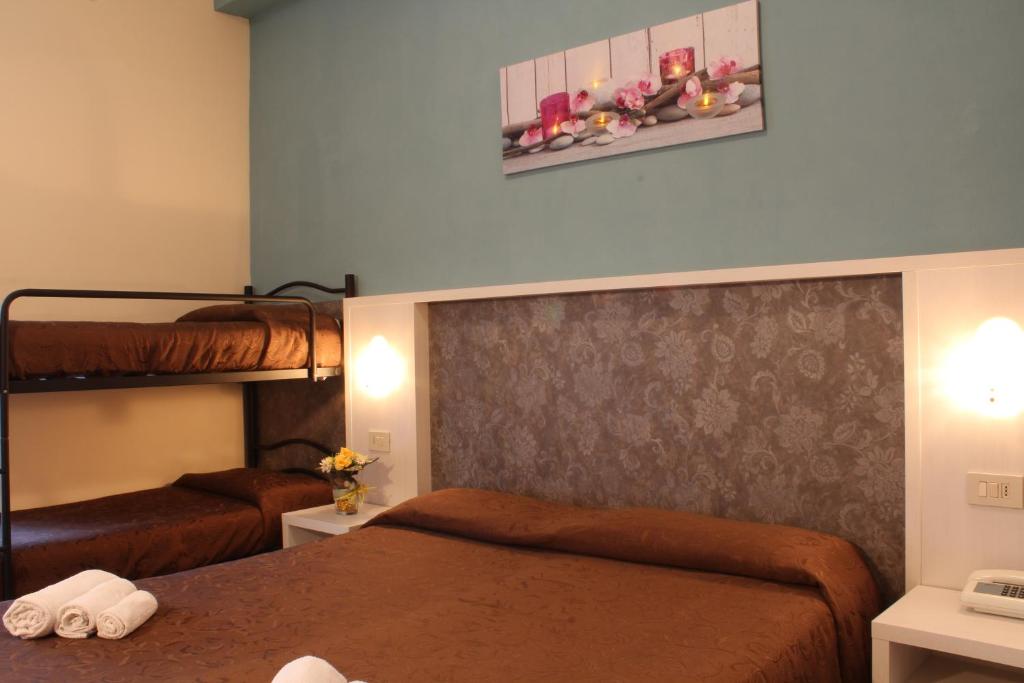 Istaba ar divām gultām un divstāvu gultu, ar brūnu tekstilu un dekoratīvu ziedu attēlu uz sienas. Gaisma un moderni interjera elementi rada mājīgu atmosfēru.