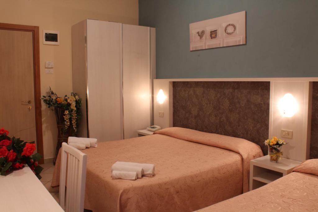 Mājīgs viesnīcas numurs ar divām gultām, gaišu apdari un dekoratīvām puķēm uz galda. Numurā ir skapji un gaismas, radot patīkamu atmosfēru.