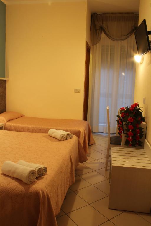 Gaismas un mājīgas viesnīcas istabas ar divām gultām, baltiem dvieļiem un ziedu kompozīciju. Telpa ir iekārtota ar moderniem elementiem un logu, kas nodrošina dabīgu apgaismojumu.