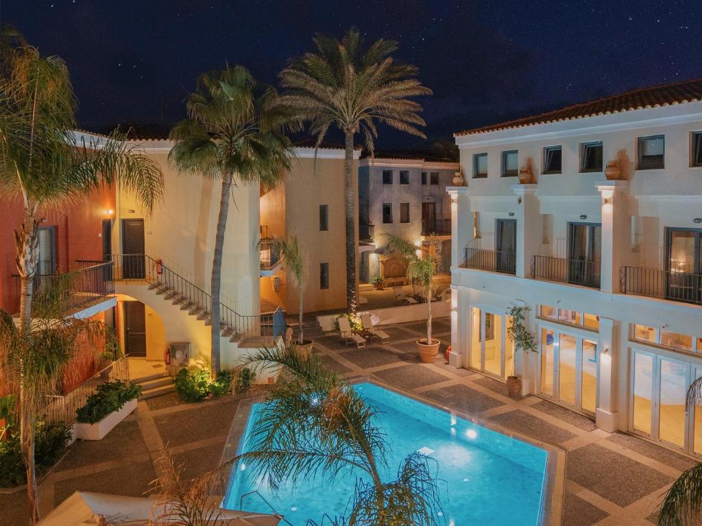 Grecotel Plaza Beach House nakts skats uz baseinu un viesnīcas arhitektūru.