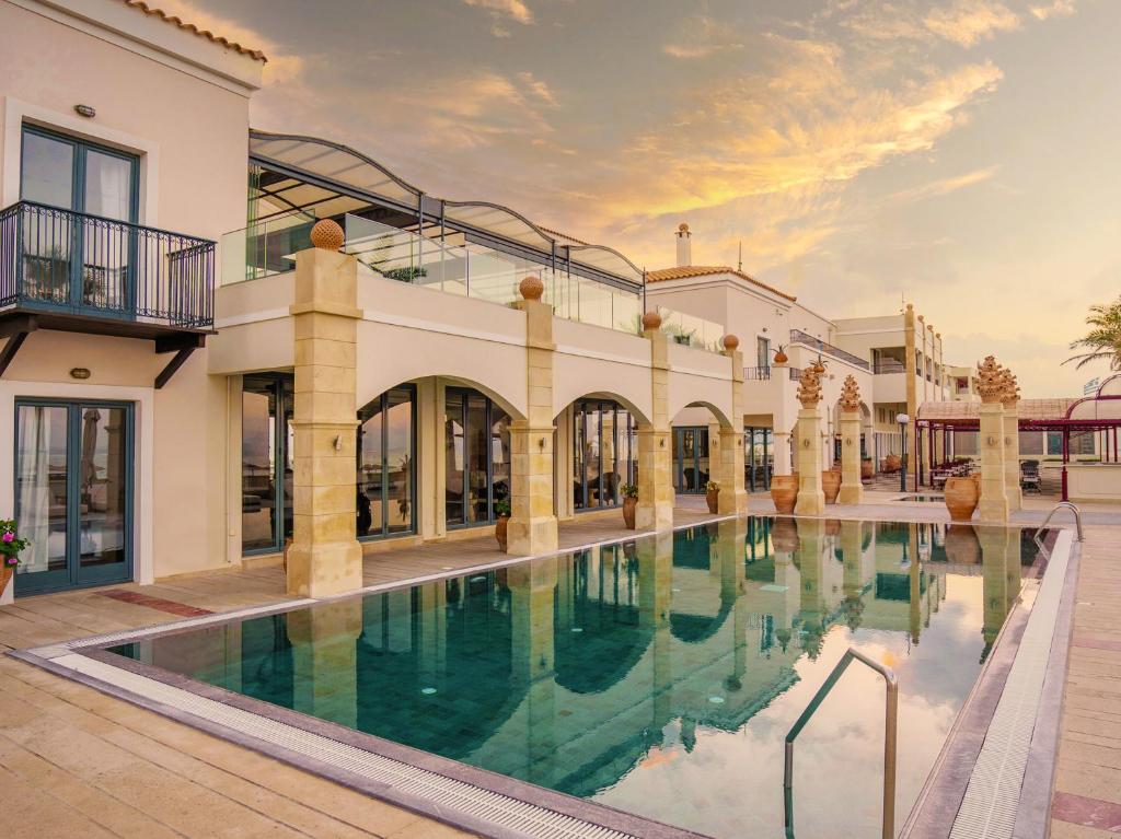 Grecotel Plaza Beach House pievienošanās baseins un arhitektūra saulainā vakarā.