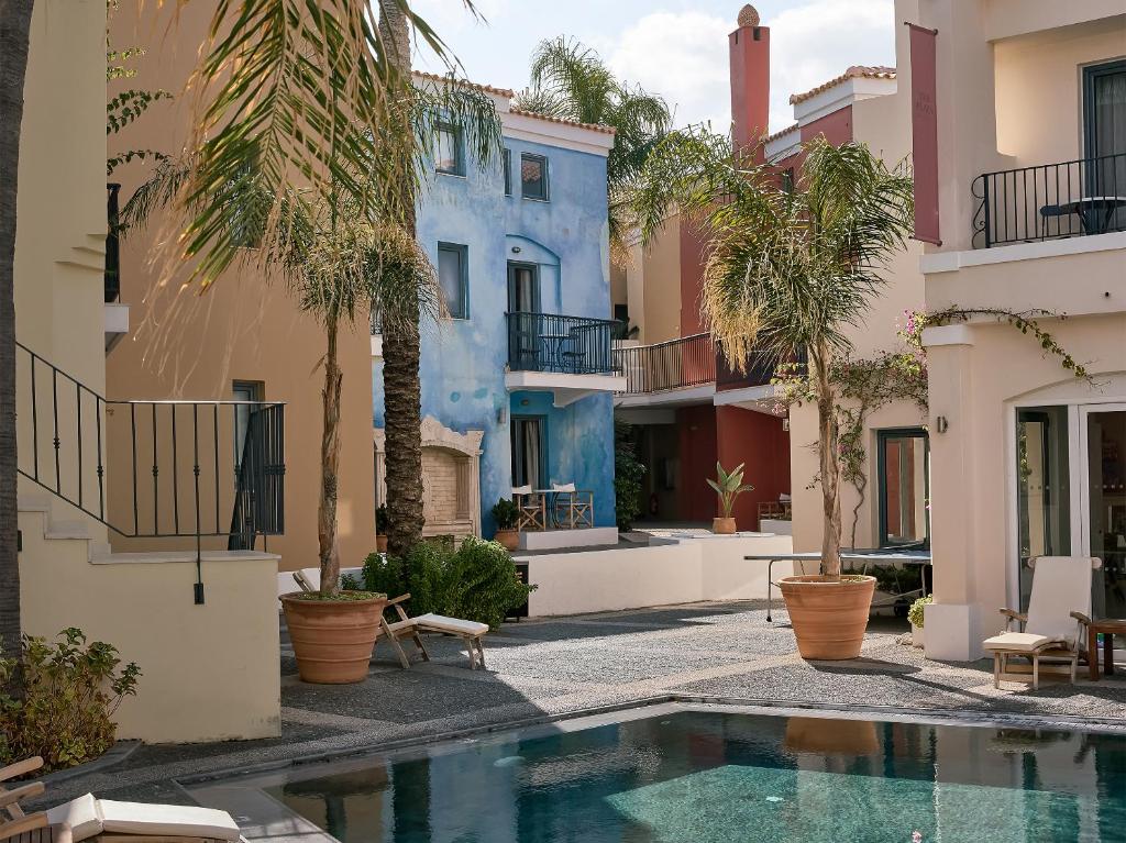 Grecotel Plaza Beach House viesnīcas ainava ar peldbaseinu un krāsainām ēkām.