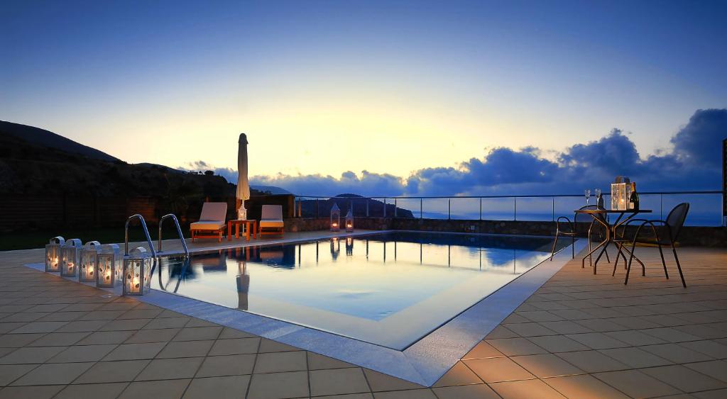 Eleganta baseina zona ar skatu uz saulrietu, kurā redzami atpūtas krēsli un gaismas laternas. Miers un relaksācija vakara noskaņā.