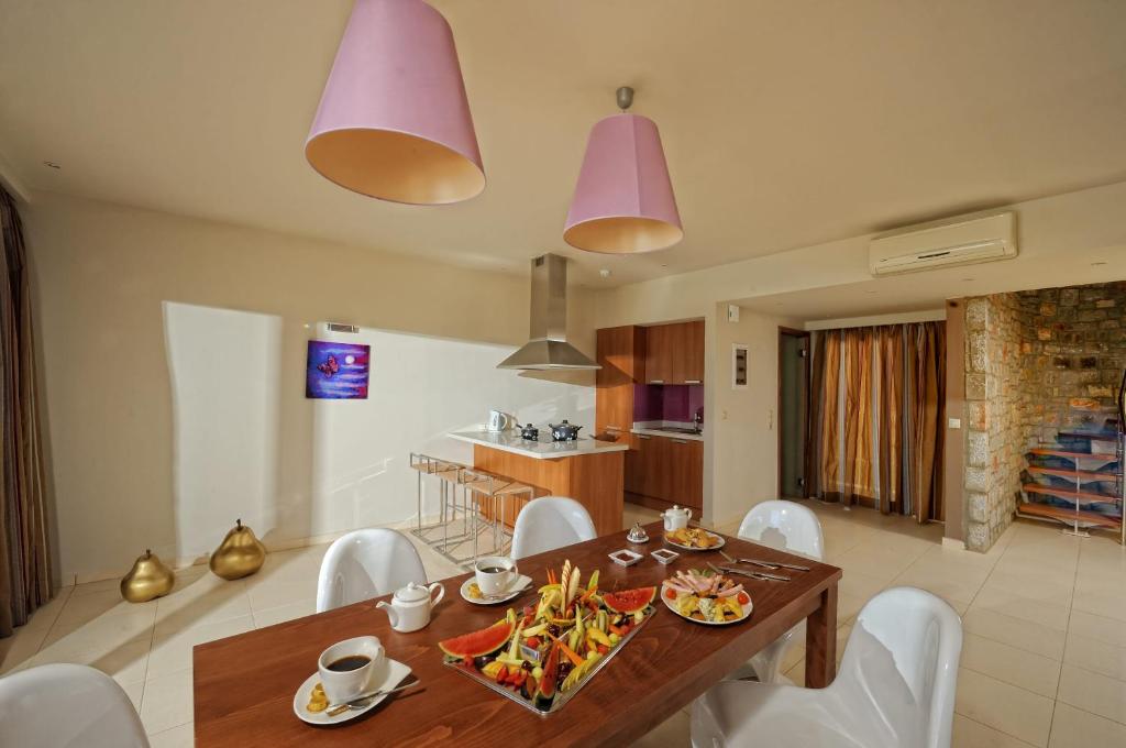 Mūsdienīga virtuve ar elegantu ēdamgaldu, uz kura ir dažādas uzkodas un dzērieni, kā arī stilīgas rozā lampas un mūsdienīga interjera elementi.