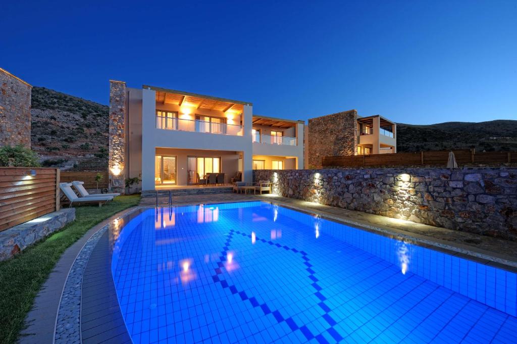 Mūsdienīga villa ar apgaismotu baseinu, kas atrodas gleznainā kalnu apkārtnē. Gaismas spīd caur logiem, radot viesmīlīgu atmosfēru.