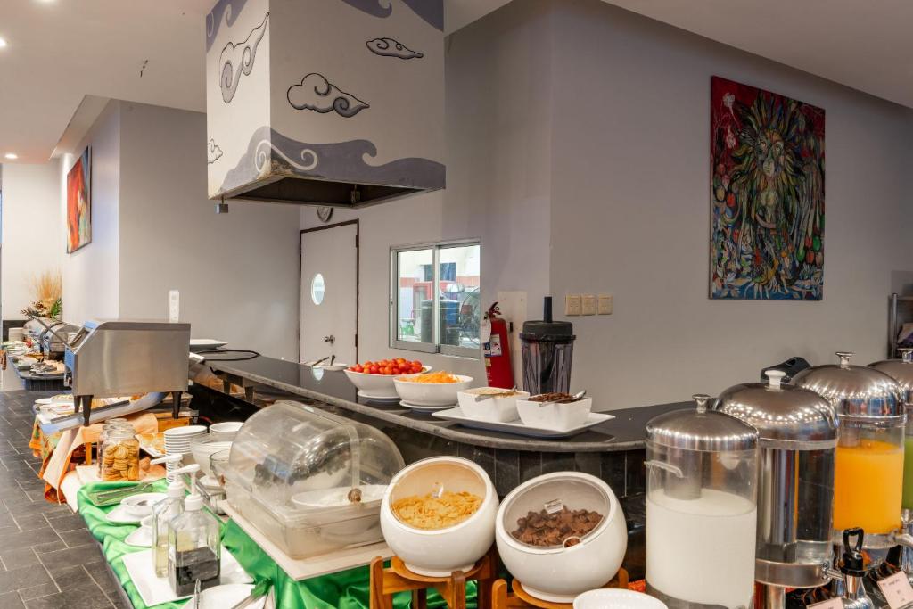 Brokastu bufete ar dažādām ēdienu izvēlēm un dzērieniem, iekārtota mūsdienīgā vidē ar mākslinieciskām gleznām uz sienām.