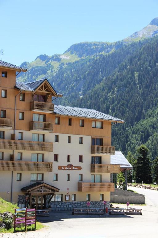 Kalnu viesnīca ar koka elementiem un balkoniem, izvietota gleznainā kalnu ainavā. Apkārt viesnīcai redzami zaļi meži un kalni, kas rada mierīgu atmosfēru.